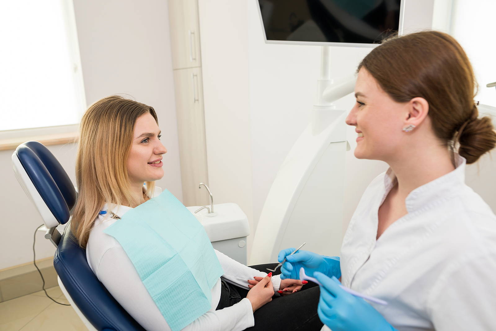 A Beautiful Female Dentist Is Talking To A Patient While Sitting A beautiful female dentist is talking to a patient while sitting in a chair.
