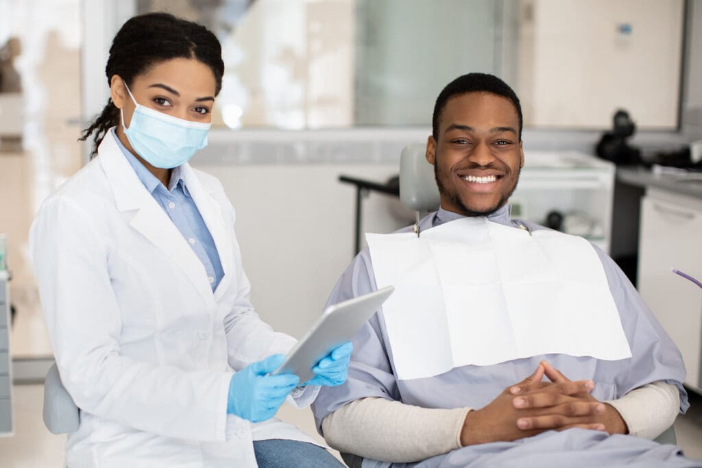 A young man sitting in a dental chair with a dental assistant next to him.